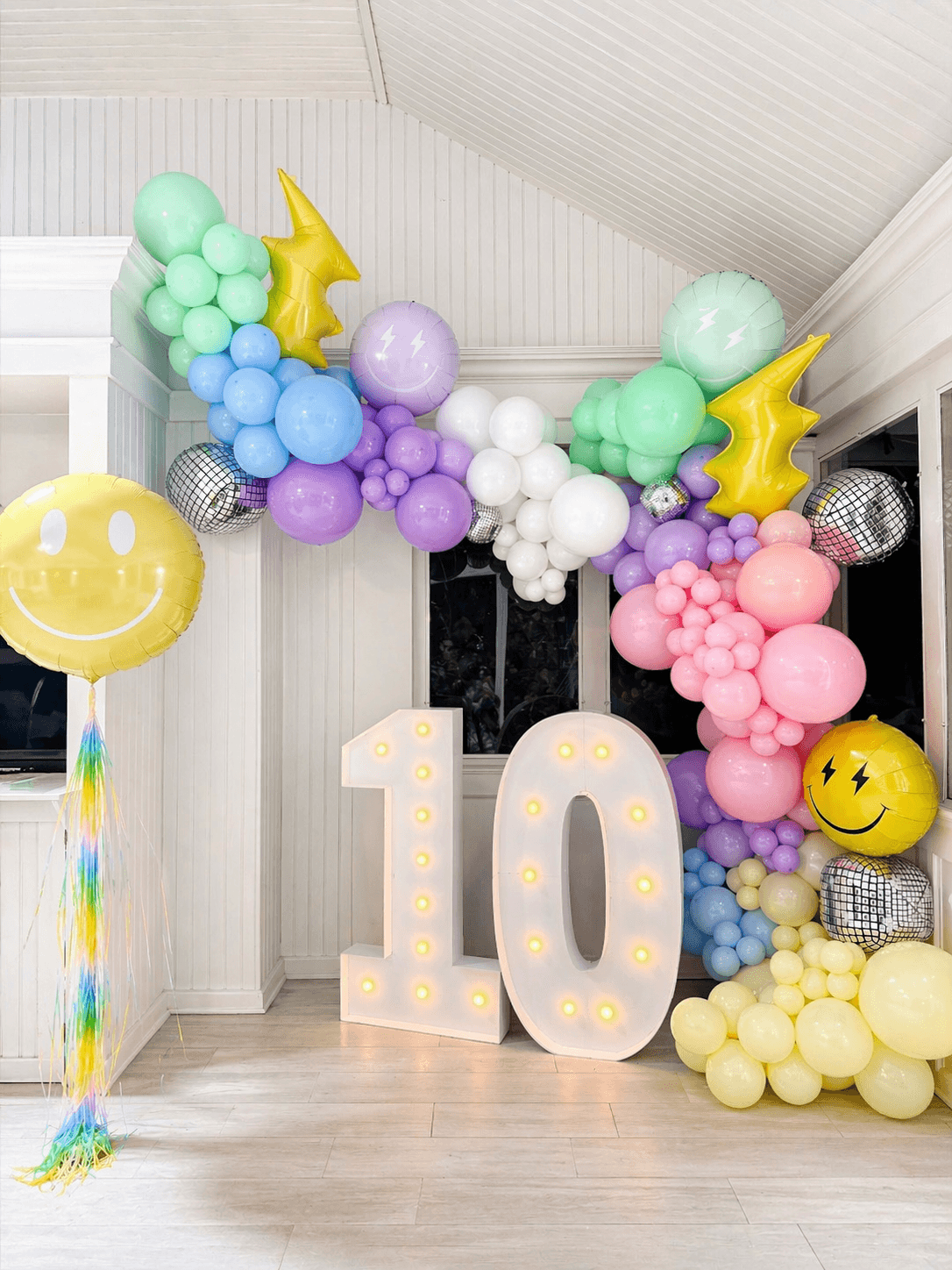 Pastel balloon installation with marquee ten numbers and smiley accents for a birthday party